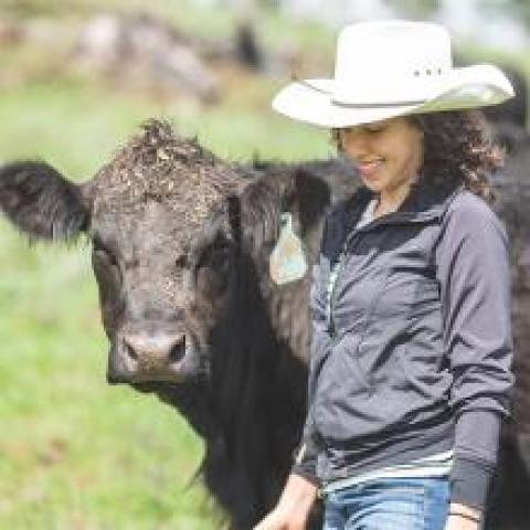 Woman wearing a cowboy hat, walking next to a cow